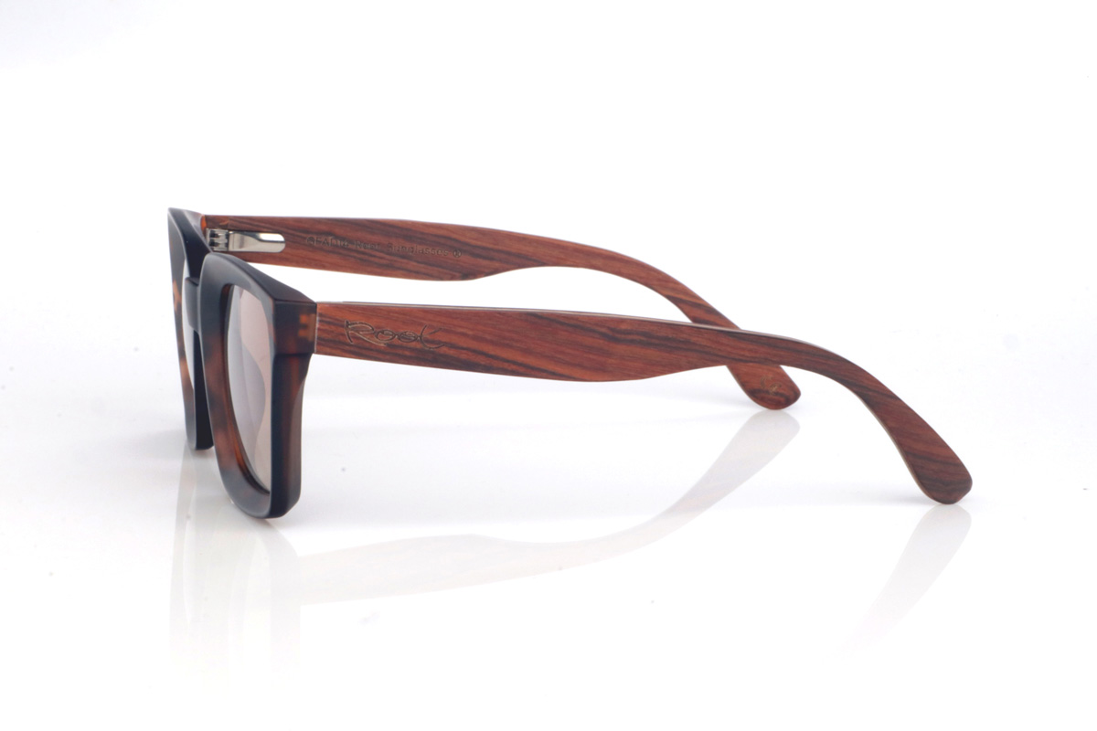 Gafas de Madera Natural de Palisandro REED. Las gafas de sol de madera REED combinan un frontal rectangular de estilo clásico con acabado efecto carey en tonos marrón y ámbar, muy fácil de llevar y con un punto elegante. El diseño tiene un contorno grueso y limpio, con una parte superior bastante recta y lentes en tono gris oscuro, que refuerzan ese look sobrio y atemporal.

Las varillas de palisandro aportan el contraste cálido de la madera natural, con una veta visible que hace que cada unidad tenga matices propios. En el lateral se aprecia el grabado de Root y una bisagra metálica integrada que suma solidez al conjunto. Un modelo cómodo y estable para uso diario, con protección completa frente a los rayos UV.

Dimensiones: 148X50MM
Calibre: 51 Venta al Por Mayor y Detalle | Root Sunglasses® 