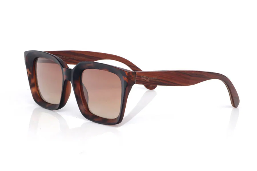 Gafas de Madera Natural de Palisandro modelo REED. Las gafas de sol de madera REED combinan un frontal rectangular de estilo clásico con acabado efecto carey en tonos marrón y ámbar, muy fácil de llevar y con un punto elegante. El diseño tiene un contorno grueso y limpio, con una parte superior bastante recta y lentes en tono gris oscuro, que refuerzan ese look sobrio y atemporal.

Las varillas de palisandro aportan el contraste cálido de la madera natural, con una veta visible que hace que cada unidad tenga matices propios. En el lateral se aprecia el grabado de Root y una bisagra metálica integrada que suma solidez al conjunto. Un modelo cómodo y estable para uso diario, con protección completa frente a los rayos UV.

Dimensiones: 148X50MM
Calibre: 51 | Root Sunglasses® 