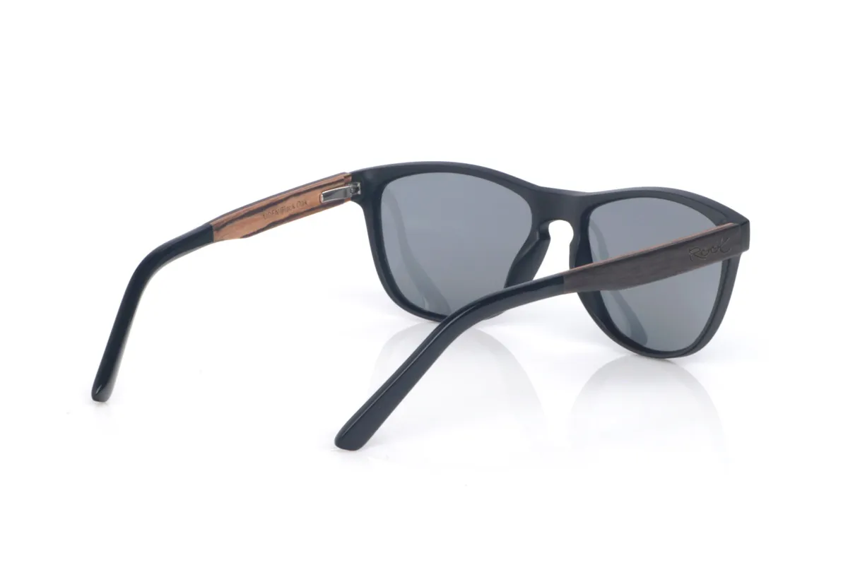 Gafas de Madera Natural de Roble AIDEN. Las gafas de sol de madera AIDEN combinan un frontal negro de acabado suave con una silueta ligeramente envolvente que equilibra presencia y comodidad. El diseño tiene líneas limpias y un contorno estilizado, con una forma entre rectangular y ovalada que favorece y resulta muy fácil de llevar en el día a día. El puente con abertura suave aporta un toque clásico y funcional, manteniendo un look moderno y sobrio.

Las varillas de roble negro añaden el contraste natural de la madera oscura, con una veta discreta que hace que cada pieza tenga matices propios. Un modelo versátil, cómodo y estable, pensado para acompañarte a diario con protección completa frente a los rayos UV.

Dimensiones: 141x49
Calibre: 54
 Venta al Por Mayor y Detalle | Root Sunglasses® 