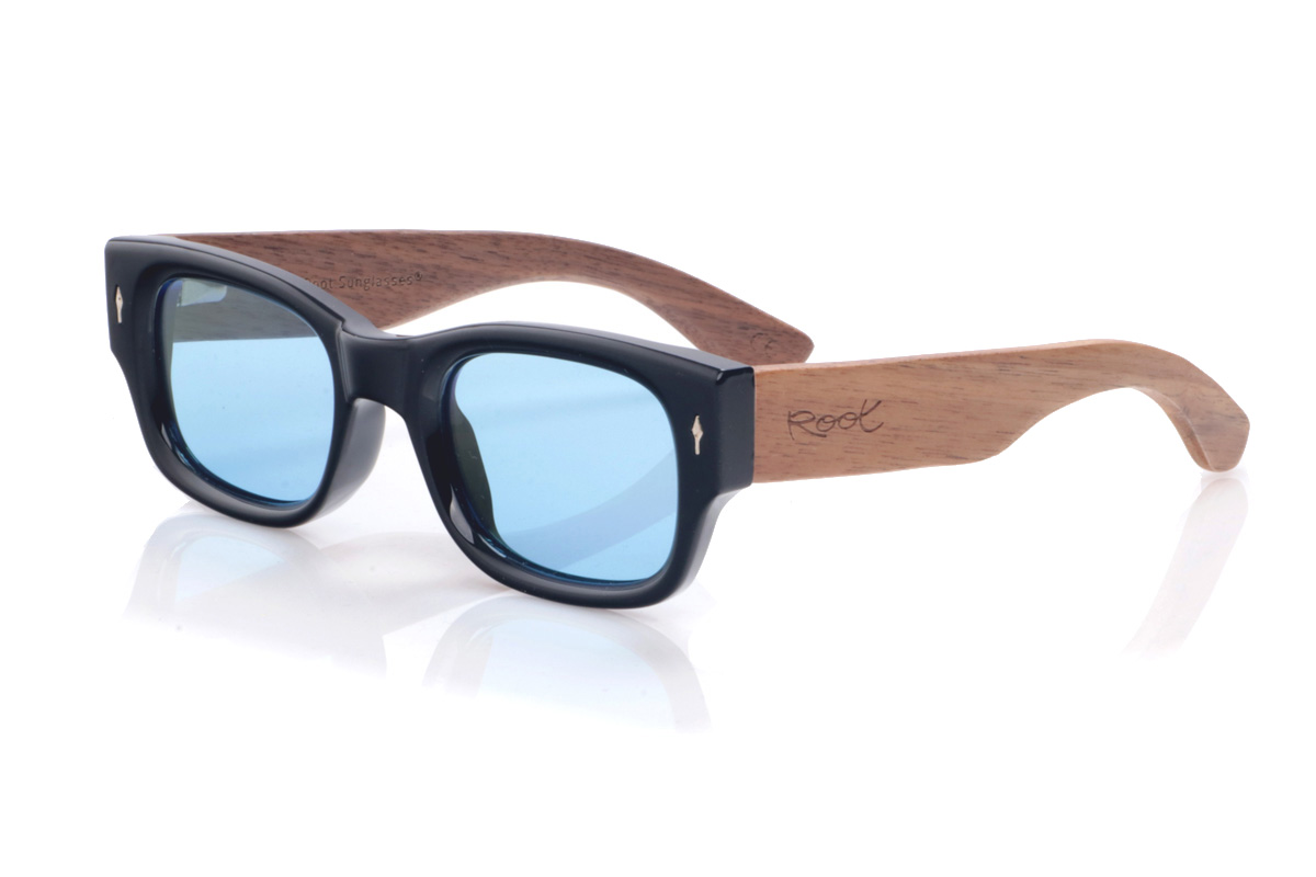 Gafas de Madera Natural de Walnut modelo BRAIL. Las gafas de sol <b>BRAIL</b> combinan un frontal negro de líneas rectangulares con varillas anchas de madera de nogal, creando un contraste potente entre lo urbano y lo natural. La montura gruesa y de perfil bajo aporta un aire retro muy marcado, mientras que las vetas cálidas del nogal y los pequeños adornos metálicos en el frontal añaden carácter a cada pieza. Su diseño unisex se adapta bien a rostros medianos, ofreciendo una sensación de solidez sin renunciar a la ligereza y la comodidad en el uso diario. Medidas: 144x45 mm. Calibre 50. | Root Sunglasses® 