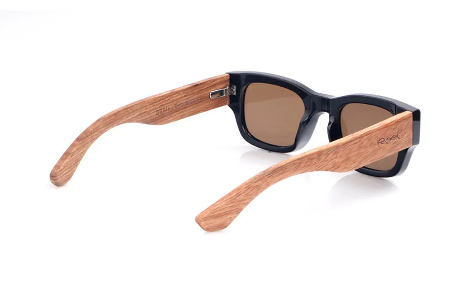Wood eyewear of Walnut BRAIL. The BRAIL sunglasses combine a rectangular black front with walnut wood temples, creating a stylish contrast between urban and natural. The thick, low-profile frame lends a distinctly retro feel, while the warm walnut grain softens the overall look and makes each pair unique. Their unisex design suits medium-sized faces well, offering a sense of solidity without sacrificing lightness and comfort for everyday wear. Equipped with polarized lenses, they reduce glare and protect your eyes from UV rays. Measurements: 144 x 45 mm. Lens width: 50. for Wholesale & Retail | Root Sunglasses® 