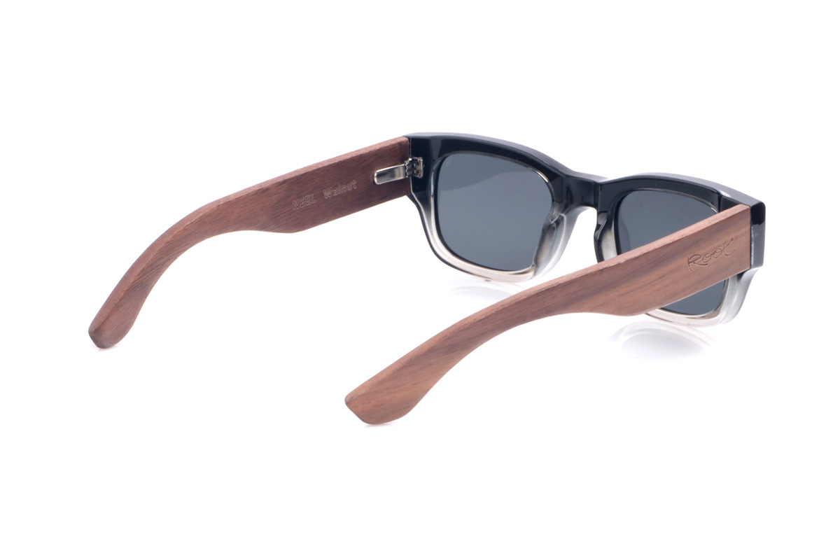 Gafas de Madera Natural de Walnut NEEL. Las gafas de sol <b>NEEL</b> combinan un frontal grueso en negro con degradado a transparente en la parte inferior y pequeños apliques metálicos en forma de flecha en las esquinas, que refuerzan su aire retro y contundente. La forma rectangular suavemente redondeada ofrece un ajuste cómodo en rostros medianos, mientras que las varillas anchas de madera de nogal muestran unas vetas cálidas y marcadas que aportan carácter artesanal y un contraste elegante con el frontal. Ligeras pese a su presencia, se sujetan con firmeza y montan lentes polarizadas oscuras que reducen reflejos y protegen eficazmente frente a los rayos UV. Medidas: 144x44 mm. Calibre 52. Venta al Por Mayor y Detalle | Root Sunglasses® 