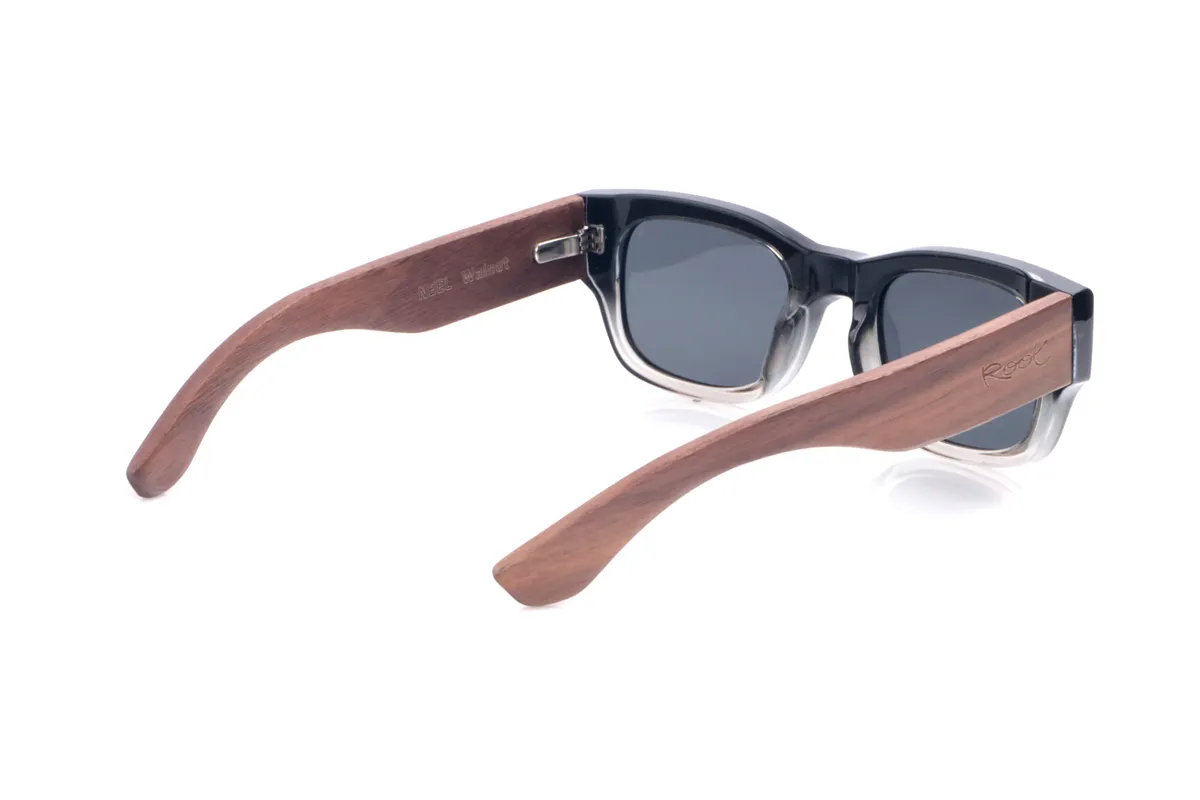 Wood eyewear of Walnut NEEL. The NEEL sunglasses combine a thick black frame with a gradient to transparent at the bottom and small metal arrow-shaped appliqués at the corners, reinforcing their bold, retro look. The gently rounded rectangular shape offers a comfortable fit for medium-sized faces, while the wide walnut temples display warm, pronounced grain that adds a handcrafted character and an elegant contrast to the frame. Lightweight despite their presence, they fit securely and feature dark polarized lenses that reduce glare and effectively protect against UV rays. Measurements: 144 x 44 mm. Lens width: 52 mm. for Wholesale & Retail | Root Sunglasses® 