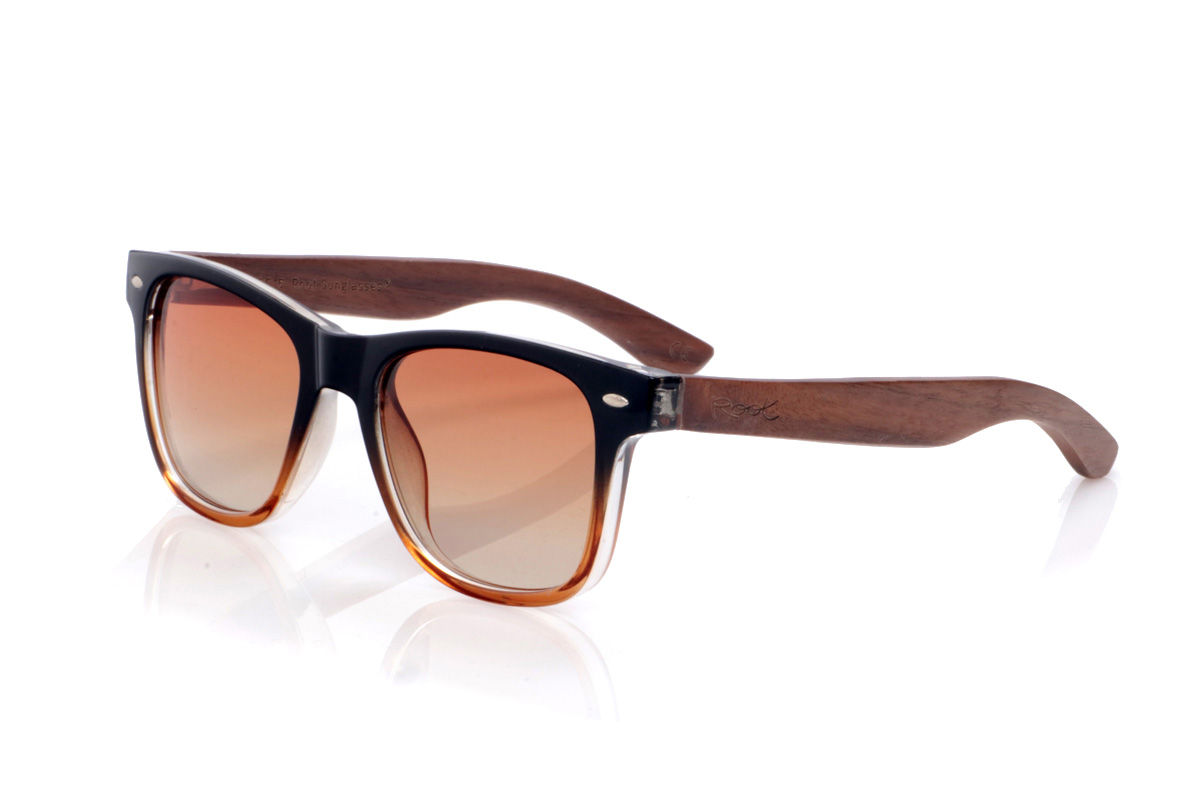 Gafas de Madera Natural de Walnut modelo DION. Las gafas de sol <b>DION</b> combinan un frontal en acetato negro con degradado ámbar en la parte inferior con unas varillas de madera de nogal, creando un contraste cálido y muy actual. Su forma clásica de inspiración wayfarer favorece la mayoría de rostros, mientras que los pequeños apliques metálicos en el frontal aportan un toque urbano y elegante. Las vetas naturales del nogal hacen que cada par sea único y, gracias a su ligereza y curvatura suave en las varillas, resultan cómodas para llevar todo el día. Incorporan lentes polarizadas degradadas que reducen los reflejos y protegen eficazmente frente a los rayos UV. Medidas: 145x49 mm. Calibre 51. | Root Sunglasses® 