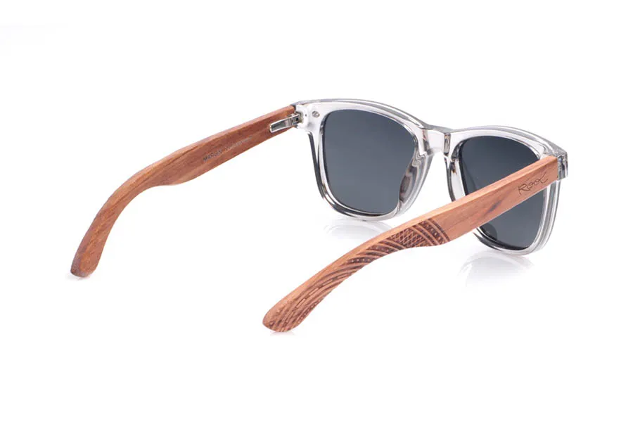 Gafas de Madera Natural de Zebrano MARLIN. Las gafas de sol <b>MARLIN</b> combinan un frontal transparente gris ahumado con varillas de madera de zebrano, que muestran vetas cálidas y naturales y rematan en unas puntas curvadas con grabado geométrico de inspiración étnica. La montura, de líneas rectas y puente marcado, mantiene una silueta clásica tipo wayfarer reinterpretada en clave ligera y contemporánea, mientras que las lentes polarizadas reducen los reflejos y ofrecen una protección eficaz frente a los rayos UV, convirtiéndolas en una opción cómoda y muy versátil para el día a día. Medidas: 143x49 mm. Calibre 50.
 Venta al Por Mayor y Detalle | Root Sunglasses® 