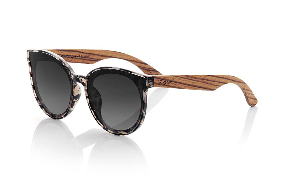 Wood eyewear of Walnut INTHIRA. INTHIRA sunglasses are the perfect complement to any feminine look. Her frontal frame in tortoiseshell shades of black, gray and cream and her rounded shape make her stand out. The lenses are mounted overexposed in the frame, giving it a very modern and attractive look. The wide temples are in grained walnut contrasting with the frame. This model is available in several lens colors, so you can choose the one that best suits your tastes and needs. With INTHIRA sunglasses, you will not go unnoticed. Front measurement approx: 142x55mmApprox front measurement: 142x55mm for Wholesale & Retail | Root Sunglasses® 