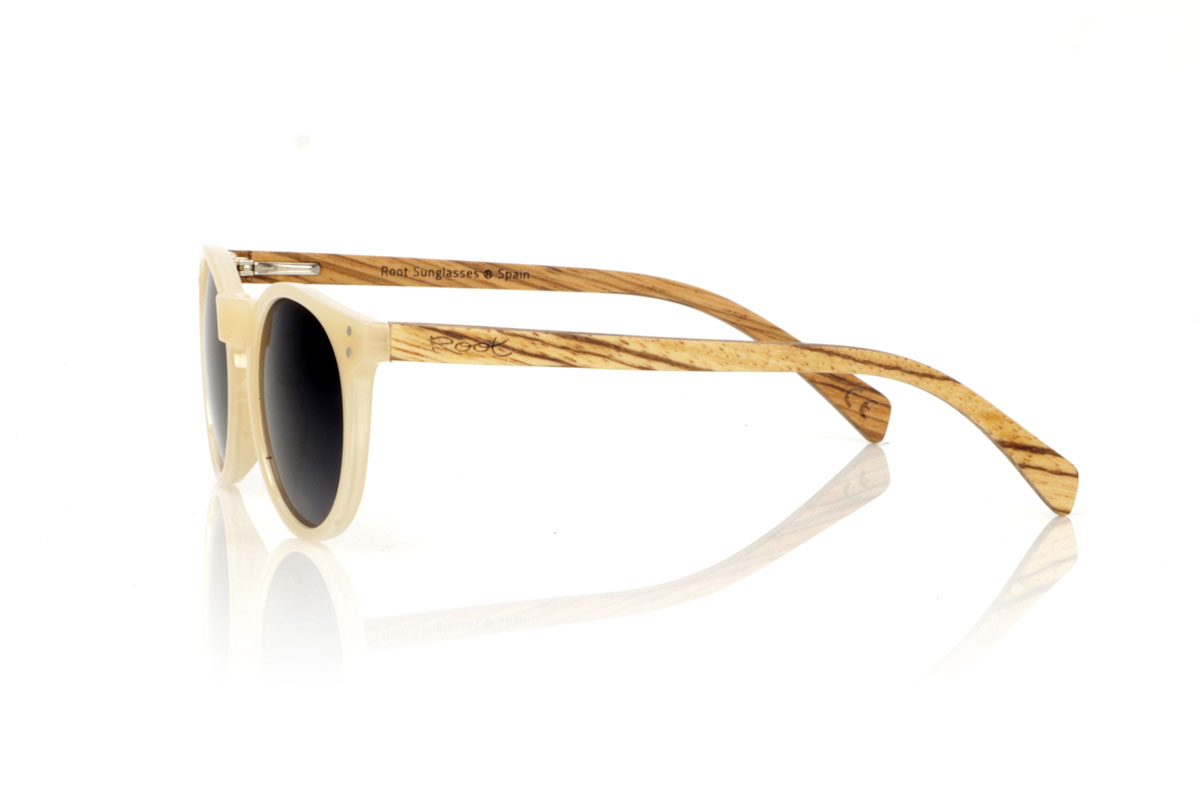 Wood eyewear of Zebrano INKY. INKY sunglasses capture the essence of a delicate and feminine design with their rounded shape and smaller size. The frame in a sophisticated satin-gloss ivory offers a touch of light and elegance, while the zebrawood temples introduce a natural and striking contrast. This model is ideal for those looking for distinctive but subtle glasses that complement without overloading. With measurements of 138x48mm and a caliber of 47, the INKY adapts perfectly to thinner faces, ensuring comfort and style. Immerse yourself in the beauty of the details to enhance your look with a unique charm. for Wholesale & Retail | Root Sunglasses® 