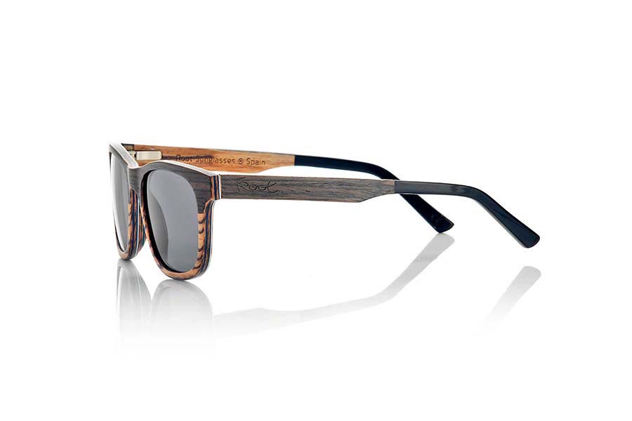 Gafas de Madera Natural de Nogal Negro NAMIB. Las gafas de sol NAMIB son el resultado de la combinación de finas láminas de madera de nogal negro con madera de zebrano. El diseño frontal se compone de la elegante combinación de madera de nogal negro en la parte superior y madera de zebrano en la inferior, y el interior de la montura es de madera de zebrano. La lámina muy fina de aluminio y la lámina coloreada azul incorporadas entre las láminas de madera del frontal aportan un toque de sofisticación. Las gafas NAMIB son un modelo anguloso de tamaño reducido, ideal para caras delgadas y afiladas, con varillas terminadas en acetato de alta calidad para permitir su ajuste en caso de ser necesario. Con solo 4.2mm de espesor y un peso de 17 gramos, son ultrafinas y ultraligeras, pero el refuerzo de aluminio las hace resistentes y duraderas. Te sorprenderá la belleza de la combinación de dos maderas en el frontal y su toque metálico en los laterales. Además, <B>disponen de sistema para montar lentes graduadas</B>.  Medida frontal: 140x46mm. Venta al Por Mayor y Detalle | Root Sunglasses® 