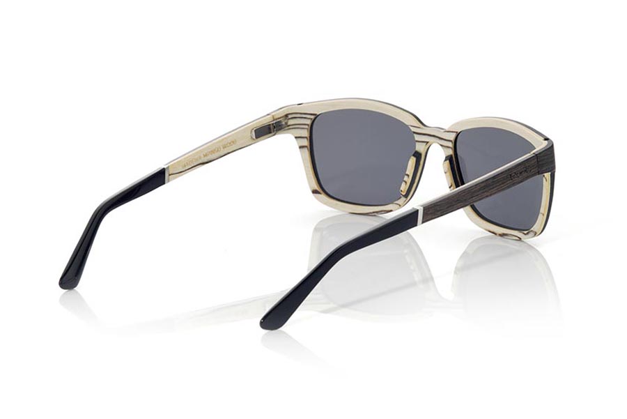 Wood eyewear of Mpingo MADEIRA. MADEIRA wooden sunglasses are an avant-garde model made of ebony and white wood, with a laminated structure with suggestive shapes and modern lines. The hinge of the temples is presented forward, which gives it an innovative and risky touch. The front of the MADEIRA is made of Mpingo laminated wood on the outside and white wood on the inside, which gives the glasses a unique beauty. The temples are also made with the same laminated pattern as the frame and are finished in acetate with a rod that allows them to be adjusted if necessary. The MADEIRA are an elegant and sophisticated model that will surprise everyone due to its combination of woods, careful finish and its very suggestive shape. Front measurement: 138x45mm. for Wholesale & Retail | Root Sunglasses® 