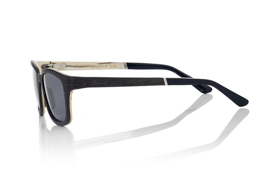 Wood eyewear of Mpingo MADEIRA. MADEIRA wooden sunglasses are an avant-garde model made of ebony and white wood, with a laminated structure with suggestive shapes and modern lines. The hinge of the temples is presented forward, which gives it an innovative and risky touch. The front of the MADEIRA is made of Mpingo laminated wood on the outside and white wood on the inside, which gives the glasses a unique beauty. The temples are also made with the same laminated pattern as the frame and are finished in acetate with a rod that allows them to be adjusted if necessary. The MADEIRA are an elegant and sophisticated model that will surprise everyone due to its combination of woods, careful finish and its very suggestive shape. Front measurement: 138x45mm. for Wholesale & Retail | Root Sunglasses® 