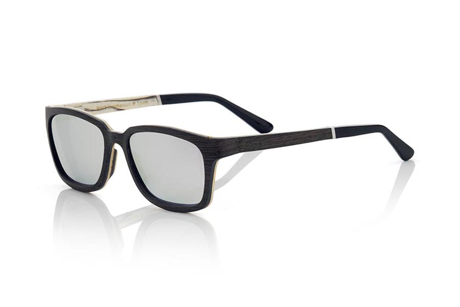 Wood eyewear of Mpingo MADEIRA. MADEIRA wooden sunglasses are an avant-garde model made of ebony and white wood, with a laminated structure with suggestive shapes and modern lines. The hinge of the temples is presented forward, which gives it an innovative and risky touch. The front of the MADEIRA is made of Mpingo laminated wood on the outside and white wood on the inside, which gives the glasses a unique beauty. The temples are also made with the same laminated pattern as the frame and are finished in acetate with a rod that allows them to be adjusted if necessary. The MADEIRA are an elegant and sophisticated model that will surprise everyone due to its combination of woods, careful finish and its very suggestive shape. Front measurement: 138x45mm. for Wholesale & Retail | Root Sunglasses® 