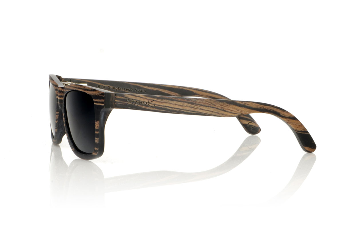 Gafas de Madera Natural de Ébano PARIS. Gafas de sol de madera PARIS presentan una silueta clásica con un toque más cuadrado y un tamaño medio, ideales para aquellos que buscan un estilo atemporal con un ajuste perfecto. Este modelo está íntegramente elaborado en madera de ébano africano, con un impresionante veteado en tonos negros y café, que aporta un aire de sofisticación. Con medidas de 148x45 y un calibre de 54, las PARIS son perfectas para quienes valoran la durabilidad y el diseño en sus accesorios. Este par no es solo un complemento para tu outfit, sino una declaración de estilo y aprecio por los detalles naturales y la artesanía de calidad. Venta al Por Mayor y Detalle | Root Sunglasses® 