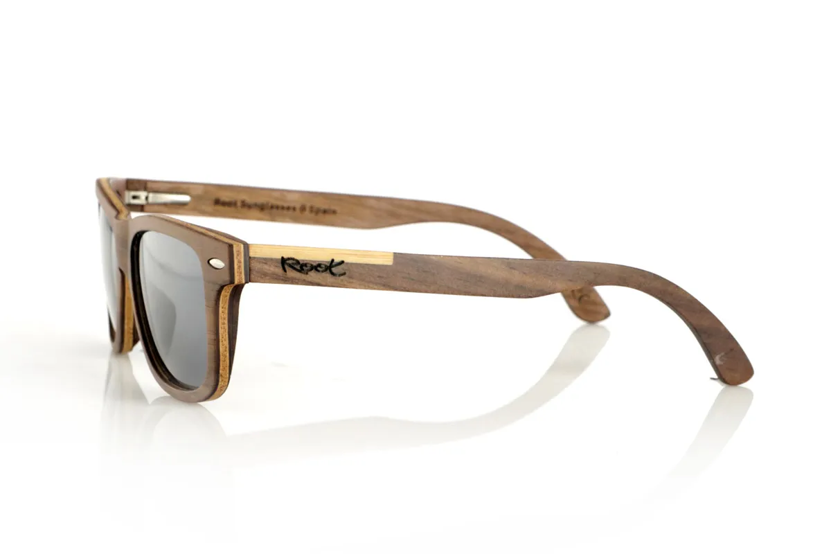 Gafas de Madera Natural de Walnut WOODSUNSET SK. Las gafas de sol de madera modelo Woodsunset están elaboradas en madera de nogal negro, ofreciendo un diseño elegante y atemporal con un acabado natural. Su estructura laminada incluye una lámina intercalada de arce natural, proporcionando un sutil contraste que realza su sofisticación.

Las patillas presentan un detalle único con una combinación de nogal y roble, aportando un toque distintivo a este modelo. Además, el frontal cuenta con pequeños adornos metálicos, que no solo refuerzan la estructura, sino que también aportan un aire vintage a su diseño.

Gracias a su forma clásica y versátil, las Woodsunset son una excelente opción tanto para hombres como para mujeres que buscan unas gafas de madera con carácter y estilo.

Medidas: 147x47 Calibre: 49 Venta al Por Mayor y Detalle | Root Sunglasses® 