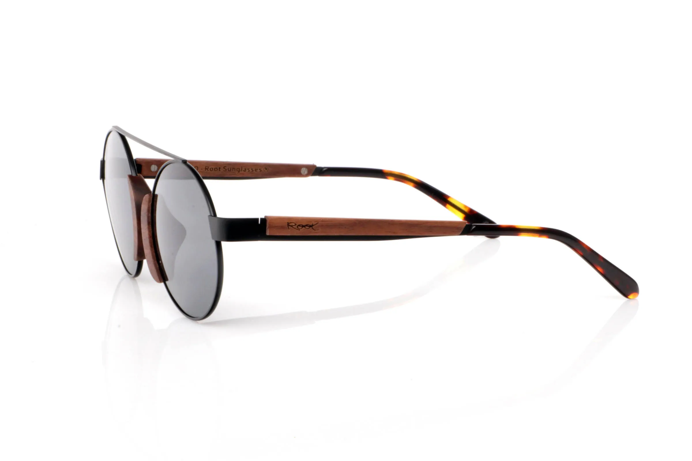 Wood eyewear of Walnut ATACAMA SK. ATACAMA SK wooden sunglasses combine a fine metal structure with walnut details that bring warmth and character. The contrast between black metal and natural wood creates a unique balance: visually light, yet full of personality.

The round shape with a top bridge recalls classic aviator-inspired forms, reinterpreted in a minimal and modern way. The walnut inserts on the front, integrated around the lenses, add a distinctive and original touch without being excessive.

They are especially comfortable thanks to their lightweight construction and flexible feel, making them ideal for long wear. The temples combine wood with tortoiseshell-style tips, adding an extra natural touch.

A subtle yet unique model, perfect for those looking for something different while keeping it simple.

Full UV protection.

Size: 128x49
Lens width: 47 for Wholesale & Retail | Root Sunglasses® 