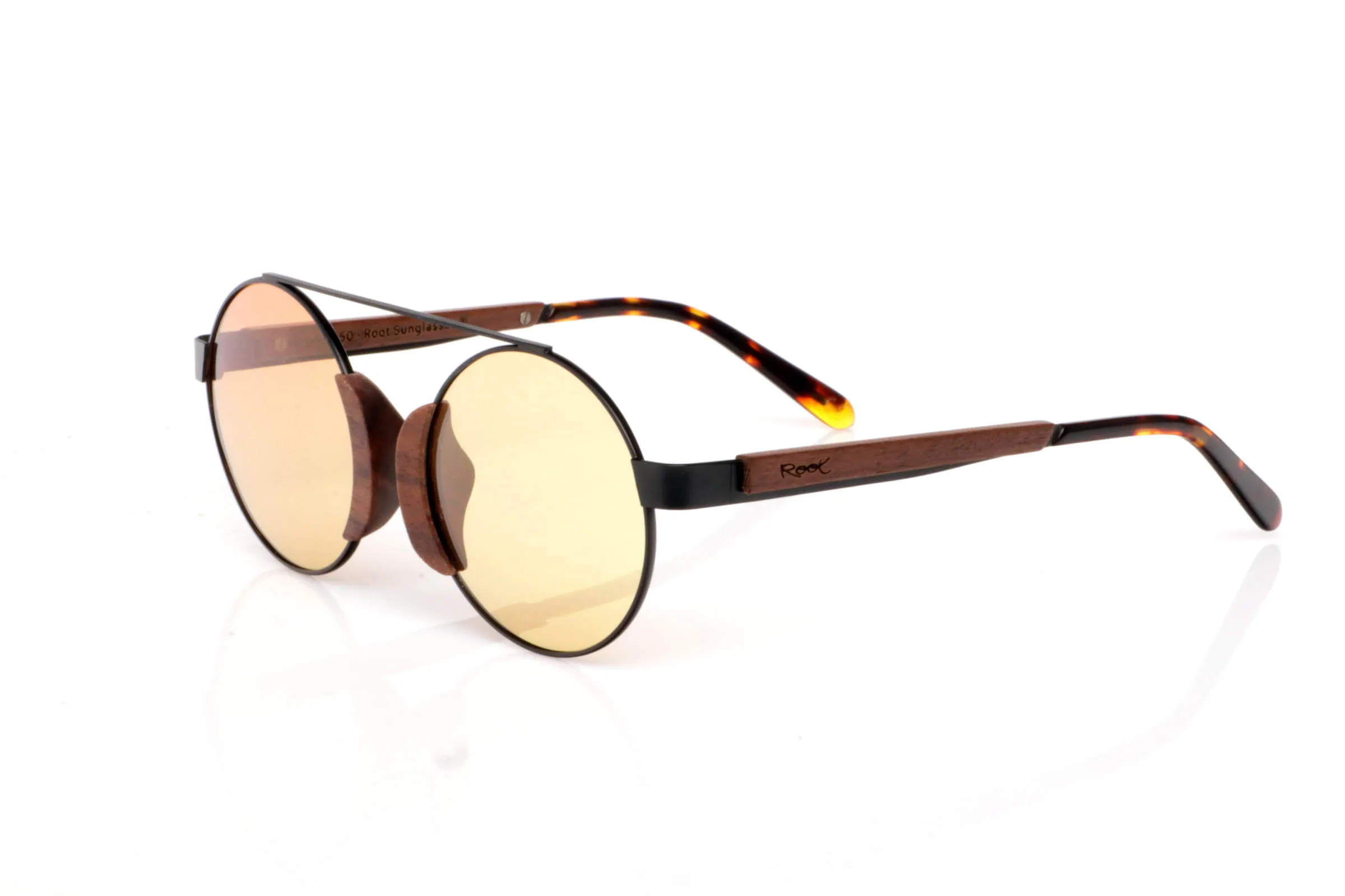 Wood eyewear of Walnut modelo ATACAMA SK. ATACAMA SK wooden sunglasses combine a fine metal structure with walnut details that bring warmth and character. The contrast between black metal and natural wood creates a unique balance: visually light, yet full of personality.

The round shape with a top bridge recalls classic aviator-inspired forms, reinterpreted in a minimal and modern way. The walnut inserts on the front, integrated around the lenses, add a distinctive and original touch without being excessive.

They are especially comfortable thanks to their lightweight construction and flexible feel, making them ideal for long wear. The temples combine wood with tortoiseshell-style tips, adding an extra natural touch.

A subtle yet unique model, perfect for those looking for something different while keeping it simple.

Full UV protection.

Size: 128x49
Lens width: 47 | Root Sunglasses® 