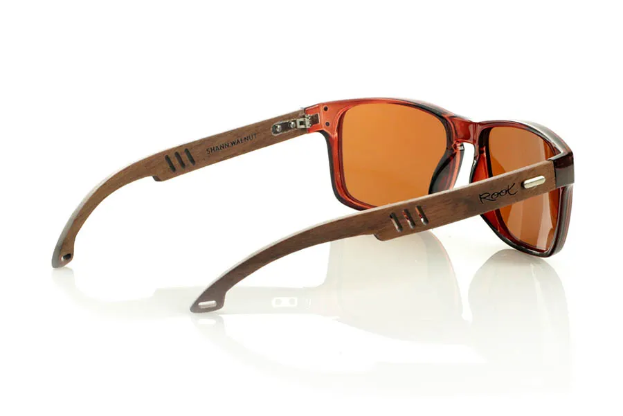 Wood eyewear of Walnut SHANN. SHANN Sunglasses with solid walnut wood temples and spring-free hardware, featuring a decorative metal detail on the exterior. The transparent brown front with a glossy finish features two metal dots on each side, reinforcing its modern and distinctive style. A sturdy, comfortable, and distinctive model, equipped with blue mirror polarized lenses and UV protection. Measurements: 146 x 48 mm. Caliber 55. for Wholesale & Retail | Root Sunglasses® 