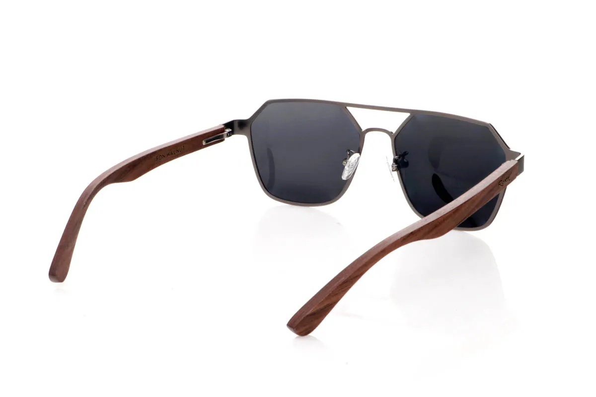 Gafas de Madera Natural de Walnut IBON. Las gafas de sol <b>IBON</b> combinan un frontal metálico de líneas geométricas con varillas de madera de walnut, creando una mezcla sofisticada entre diseño moderno y calidez natural. Su forma angular, con doble puente abierto y estructura ligera al aire, aporta un estilo atrevido y muy actual, ideal para quienes buscan unas gafas con presencia sin resultar pesadas. Las varillas de madera, finas y curvadas, muestran vetas naturales que hacen que cada par sea único y aportan comodidad durante el uso diario. Equipadas con lentes polarizadas que reducen los reflejos y protegen eficazmente frente a los rayos UV, son unas gafas diferentes, elegantes y con carácter propio. Medidas: 145x50 mm. Calibre 54. Venta al Por Mayor y Detalle | Root Sunglasses® 